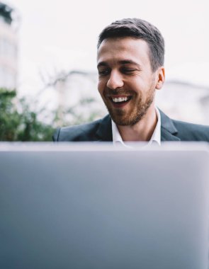 Gülümseyen akıllı iş adamı cep telefonuyla sokak kafeteryasında dizüstü bilgisayarla açık havada şirket projesinde çalışıyor.