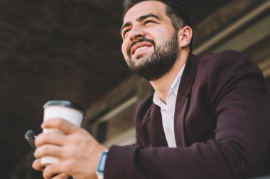 İspanyol patronun içki içme açısı düşük ve modern akıllı telefon diğer tarafa bakıyor ve modern bina terasına yaslanırken gülümsüyor.