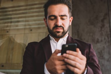 Şehrin modern binasının camına yaslanırken modern akıllı telefon kullanan şık takım elbiseli, düşük açılı İspanyol erkek.