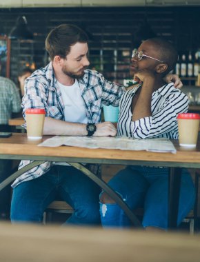 Kot pantolonlu çok ırklı bir çift şehrin karşısındaki kafede kahve içiyorlar.