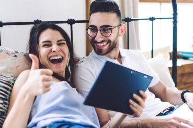 Dijital tableti tutan, gözlüklü yetişkin bir adamın yanında uzanan, dizlerinde dizlerinde dizlerinde dizleri olan, gülen bir kadın.