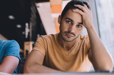 Aşağıdaki yorgun genç üniversite öğrencileri kameraya bakıyor ve modern kafede birlikte otururken üniversite ödevleriyle ilgili sorunlar yaşıyorlar.