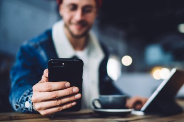 Çatı katında tablet ve bir bardak içkiyle masada otururken mesajlaşmak ve iletişim kurmak için modern dijital aletle internette sörf yapan mutlu adam.