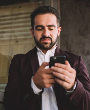 Şehrin modern binasının camına yaslanırken modern akıllı telefon kullanan şık takım elbiseli, düşük açılı İspanyol erkek.