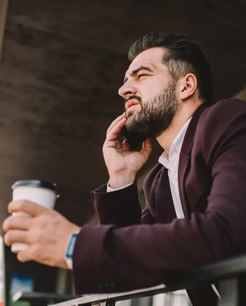 Serious male entrepreneur in formal wear concentrated during mobile phone conversation during coffee break, handsome prosperous man lawyer making smartphone call talking about case on break