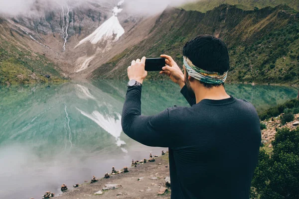 Man tourist dressed in active wear making photo of amazing reflection lake in mountains using modern smartphone device during exciting wanderlust, male traveller taking pictures of nature via mobile