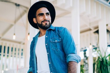 Akıllı telefonlu pozitif sakallı İspanyol adam. Elini cebine atıyor ve sokakta rahat bir restoranın önünde dikiliyor.