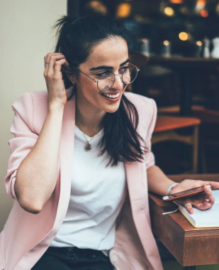Gündelik giysiler ve gözlüklerle gülümseyen çekici bir etnik kadın. Arkadaşlarıyla cep telefonu mesajlaşmaları, not defterindeki notları okuması, kafedeki saçları düzeltmesi.
