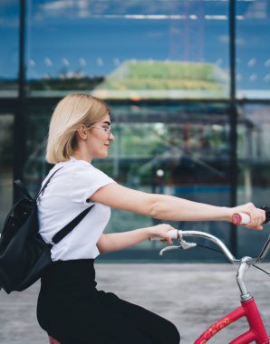 Siyah sırt çantalı, bisiklet süren ve sokakta gezen hoş sarışın bir kadın.