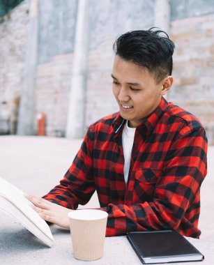 Gülümseyen Asyalı zeki içerikli öğrenci elinde kahveyle büyüleyici bir hikaye okumaya gidiyor. Şehirdeki edebiyat dersine hazırlanırken dikkatli bir şekilde.