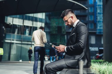 Ekrana konsantre olan ve şehir merkezindeki bankta otururken akıllı telefon kullanan düşünceli, kendini işine adamış bir çalışanın bakış açısından.