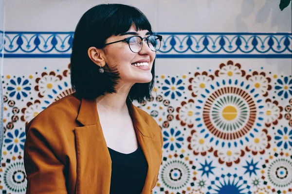 Gündelik giyim ve gözlük takan neşeli serbest yazar, bilgisayar kullanıyor, not defterindeki notları okuyor, kafede oturup başka yere bakıyor.