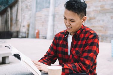 Gülümseyen Asyalı zeki içerikli öğrenci elinde kahveyle büyüleyici bir hikaye okumaya gidiyor. Şehirdeki edebiyat dersine hazırlanırken dikkatli bir şekilde.