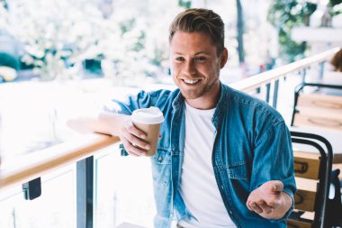 Neşeli adam günlük giysiler içinde ekin arkadaşlarıyla konuşuyor kahve içiyor güneşli bir günde kafede çitlere yaslanıyor.