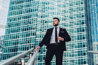 Takım elbiseli başarılı bir işadamının merdivenlerden aceleyle inerek dev modern iş merkezinin önüne bakmasından.