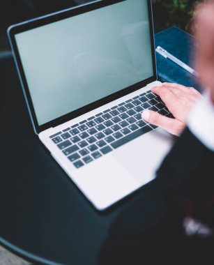 Masada defter ve kalemle yazı yazan koyu renk takım elbise uzmanının modern dizüstü bilgisayarından.