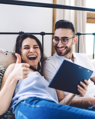 Dijital tableti tutan, gözlüklü yetişkin bir adamın yanında uzanan, dizlerinde dizlerinde dizlerinde dizleri olan, gülen bir kadın.