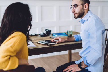 Gözlüklü, kendine güveni tam ve pozitif bir adam. Yeni iş projesinin detaylarını tartışan gündelik giysiler içindeki kadın girişimciyi dikkatle dinliyor.