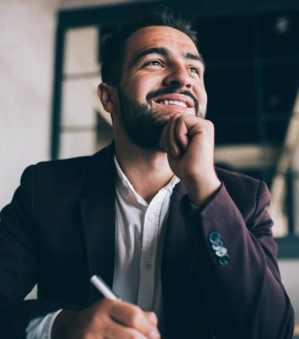 Heyecanlı, karizmatik, zarif takım elbiseli, elinde kalemle iş yerinde yüzünü çevirerek çenesine dokunan bir proje yaratan bir adamdan.