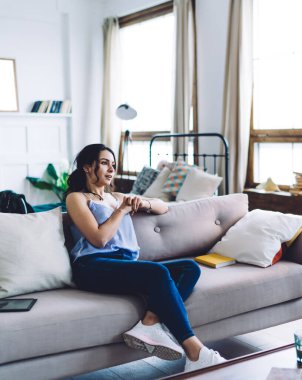 Beyaz tişörtlü ve kot pantolonlu yakışıklı bir erkek kol saatini gösteriyor ve çağdaş oturma odasındaki kanepede oturan genç bir kıza acele etmesini söylüyor.