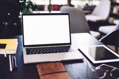 Ofisteki siyah masada boş ekranlı yeni dizüstü bilgisayar tabletli ve bulanık arkaplanda gözlüklü defterlerin yanında