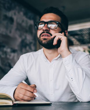 Ciddi sakallı hippi kahve dükkanında çalışma planlarını kontrol etmek için cep telefonu konuşması yapıyor. Gözlüklü genç girişimci cep telefonuyla bilgi yazıyor.