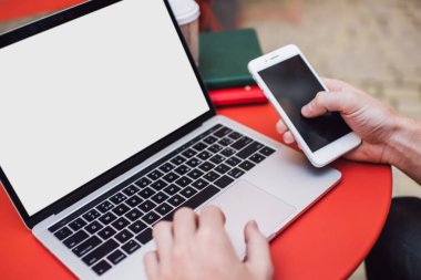 Cep telefonu tutan ve sokak kafesindeki masada otururken boş ekranla dizüstü bilgisayarda yazan yüzsüz serbest yazardan.