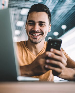 İş yerindeki masada oturan, arkadaşlarıyla cep telefonu sohbeti yapan, günlük kıyafetli, pozitif bir adamdan.