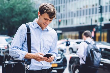 Ofisteki gülümseyen yakışıklı işçi giysisi ve büyük deri çantalı kulaklıkla sokakta yürürken telefonla mesajlaşıyor.