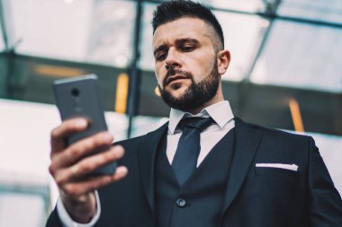 Modern şehrin merkezindeki çağdaş bir binanın önünde dikilirken, takım elbiseli, kaşlarını çatan ve akıllı telefonlara bakan iş adamlarından.