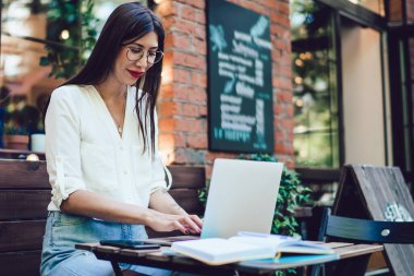Optik gözlüklü milenyum öğrencisi üniversite dersleri için dijital bilgi araştırması yapıyor. İnternet sitelerini taramak için internet bağlantısı olan sokak kafeteryasında oturuyor.