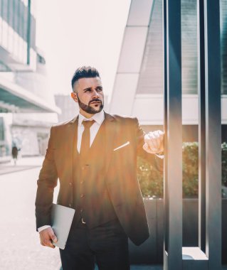 Tabletli akıllı sakallı patron güneşli bir günde metal sütunların yanında dikilirken başka yere bakıyor ve düşünüyor.