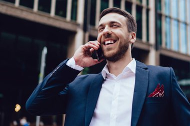 Resmi olarak iyimser girişimcinin düşük açısı gülmek ve şehrin bulanık arka planında dikilirken akıllı telefon konuşması yapmak.