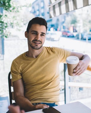 Rahat giyinen adam, kafeteryada çitlere yaslanmış bir fincan kahve içen hasatçı ile iletişim kuruyor.