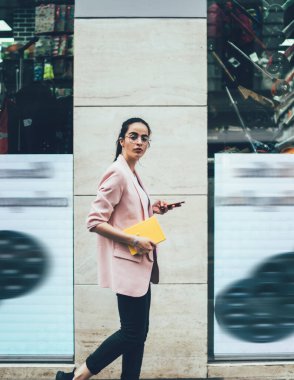 Günlük kıyafetlerle ve not defteriyle gezen genç bir bayanın yan görüntüsü. Arkadaşlarıyla telefonda mesajlaşıp kameraya bakıyorlar.