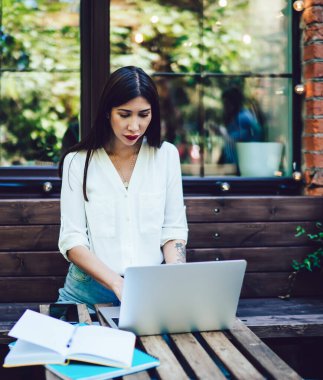 Ciddi genç yönetici, birlikte çalışan sokak kafesinde çağdaş bir dizüstü bilgisayar üzerinde çalışıyor, hipster kız sosyal medya ağında iletişim kurarak bilgi topluyor.