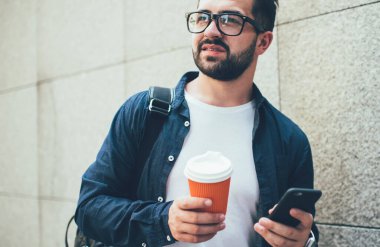 Gündelik kıyafet ve gözlüklü yakışıklı beyaz adam sokakta cep telefonu kullanıyor. Düşünceli erkek öğrenci cep telefonuyla posta yolluyor. Şehir merkezine gitmek için kahve getiriyor.