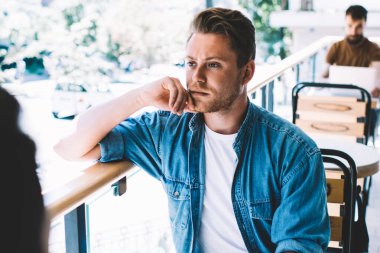 Çitlere yaslanmış, çitlere dokunmuş, düşüncelere dalmış kafeteryada oturan ekin arkadaşlarıyla gevşeyen yakışıklı bir erkek.