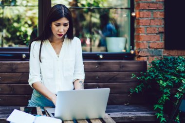Ciddi genç yönetici, birlikte çalışan sokak kafesinde çağdaş bir dizüstü bilgisayar üzerinde çalışıyor, hipster kız sosyal medya ağında iletişim kurarak bilgi topluyor.