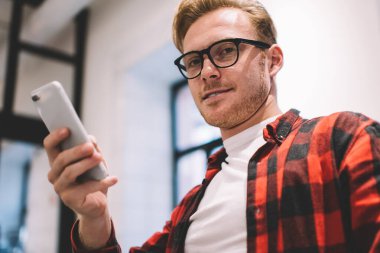 Düşünceli, sakin, stil sahibi, kahveli serbest çalışan, iş yerinde kameraya bakarken cep telefonu kullanarak haber okuyan biri.