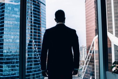 Modern ofisin panoramik penceresinden şehir merkezine bakarken başarılı, düşünceli bir işadamının karar verişi.