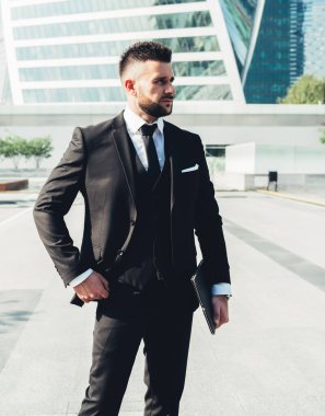 Siyah takım elbiseli yakışıklı bir erkek, parlak güneşin altında modern şehrin caddesinde duran meslektaşıyla buluşmayı bekliyor.