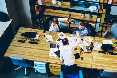 Resmi giyinmiş ve gözlüklü siyahi adamın başarılı bir projenin keyfini çıkarırken, iş yerinde partnerler beşlik çakıyor.