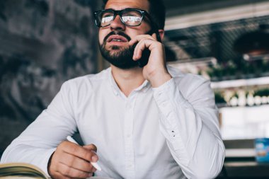 Ciddi sakallı hippi kahve dükkanında çalışma planlarını kontrol etmek için cep telefonu konuşması yapıyor. Gözlüklü genç girişimci cep telefonuyla bilgi yazıyor.