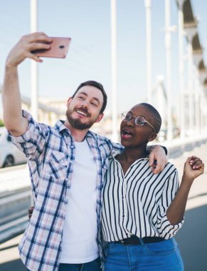 Gülümseyen sakallı adam görüntülü sohbetten arkadaşını arıyor. Afrikalı Amerikalı içerikli gözlüklü, kısa saçlı genç bayanı kucaklıyor.