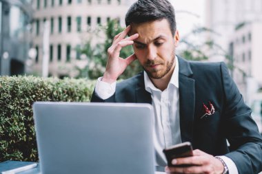 Odaklanmış, cep telefonlu, dizüstü bilgisayarı olan ve kafeteryada iş planıyla ilgili fikirler üreten adam.