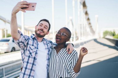 Gülümseyen sakallı adam görüntülü sohbetten arkadaşını arıyor. Afrikalı Amerikalı içerikli gözlüklü, kısa saçlı genç bayanı kucaklıyor.