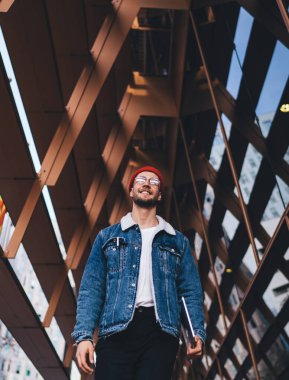 Tablet taşıyan ve şehir merkezinde modern cam gökdelenlerle gezen modaya uygun giyinmiş neşeli bir adamdan.