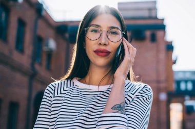 Gözlüklü çekici bir kızın yarı boy portresi. Şehir sokağındaki boş zamanlarında kameraya bakıyor. 4 g 'lik interneti telefonla kullanan güzel bir kadın.