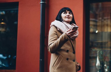 Sıcak giyimli, rüya gibi bir genç hanım, cebinde cep telefonuyla arkadaşlarıyla sohbet ediyor.